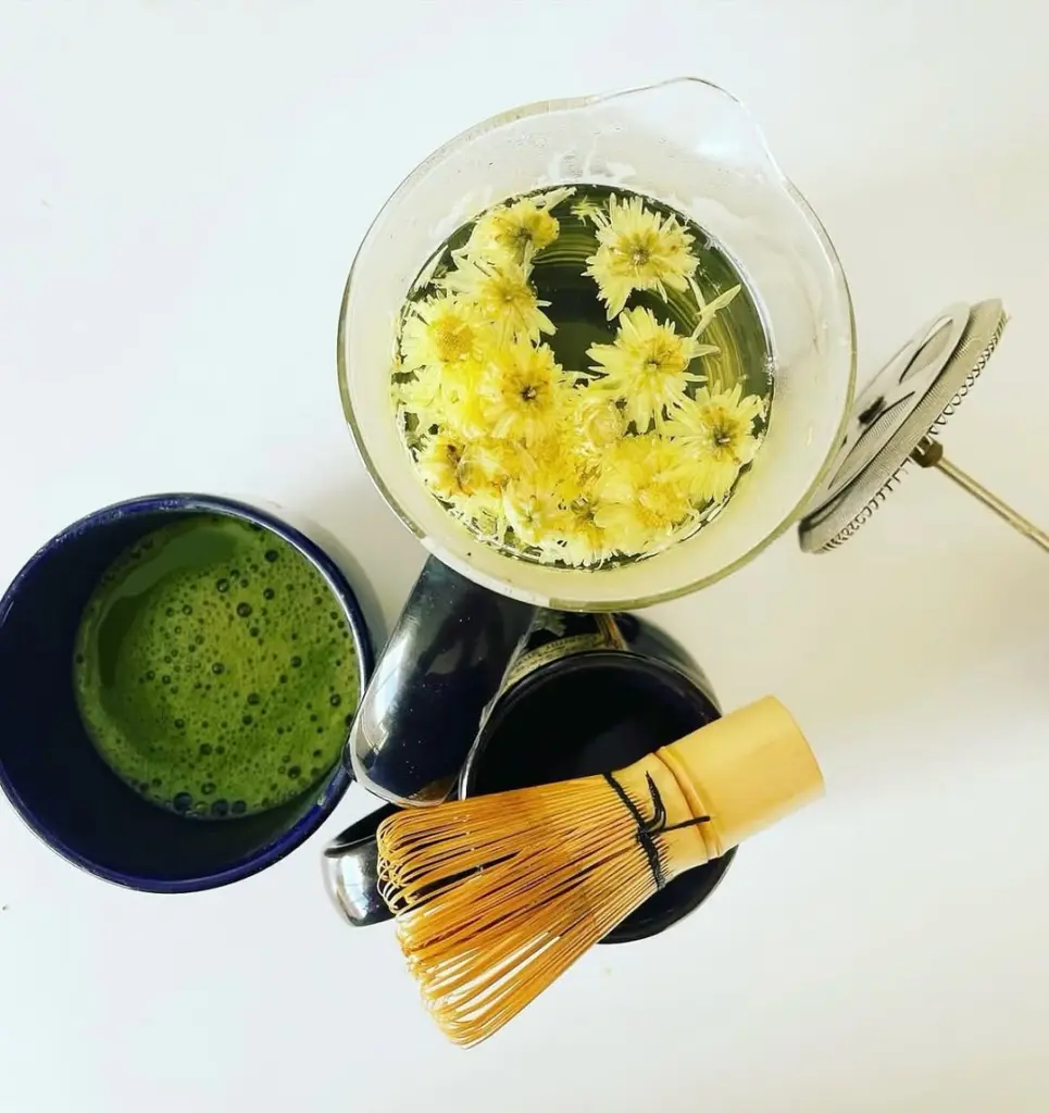 Bowl of frothy matcha beside a bamboo whisk and glass vessel of yellow flowers