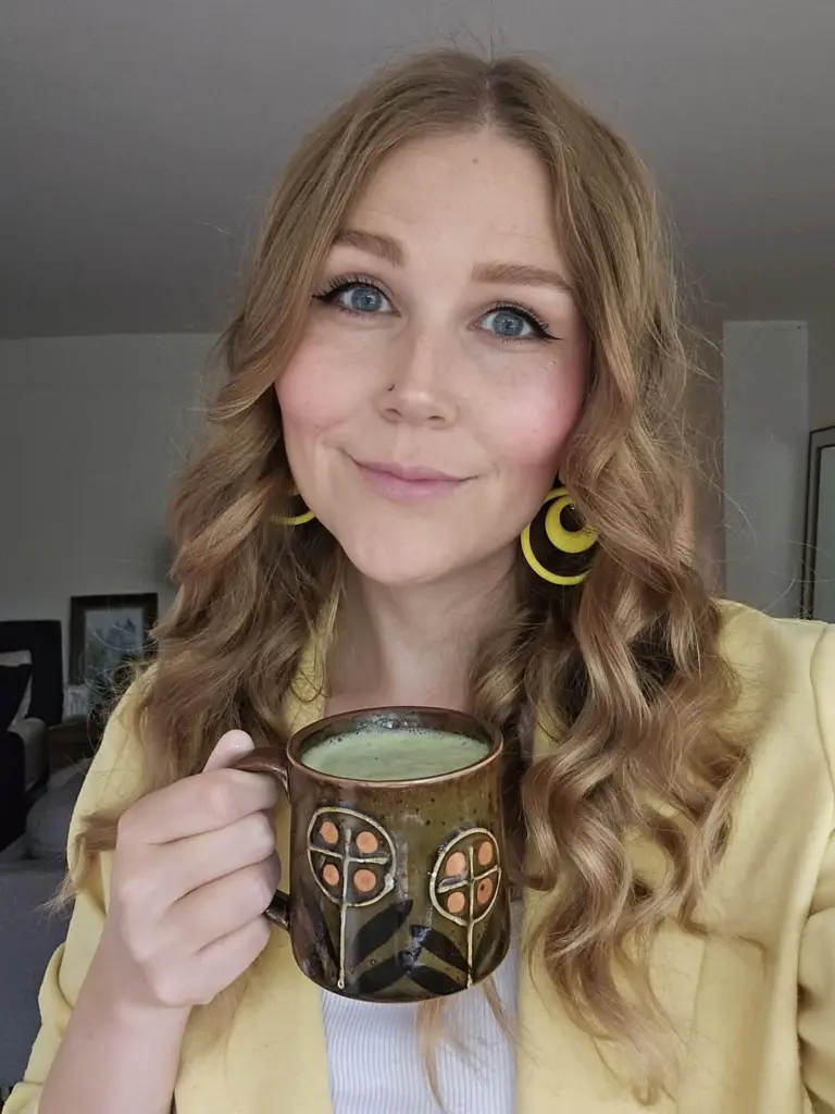 Smiling woman holding a ceramic mug filled with a frothy green drink