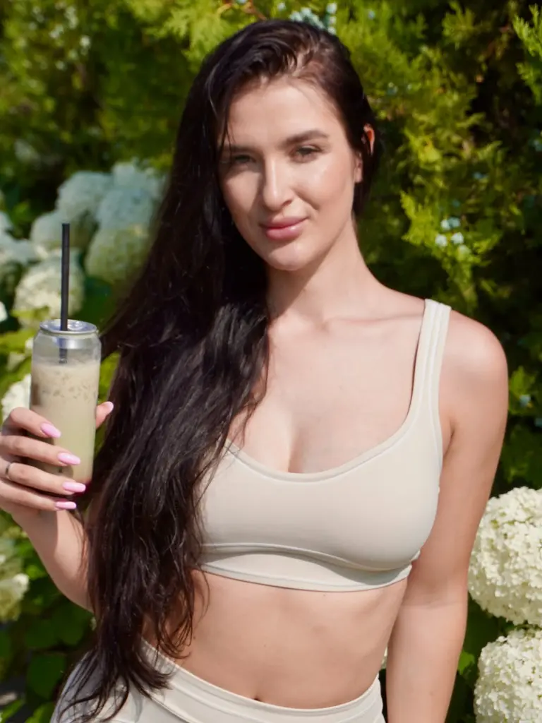 Woman holding a pale iced drink in front of white hydrangeas