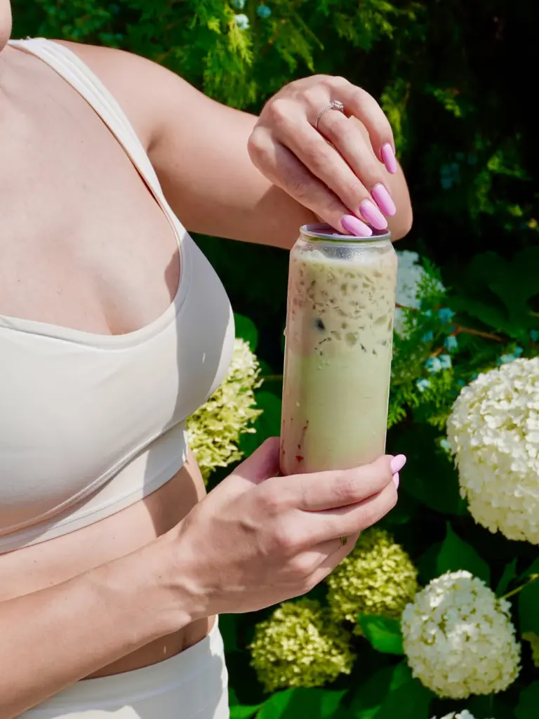 Hands opening a tall can-shaped glass filled with a pale green iced drink