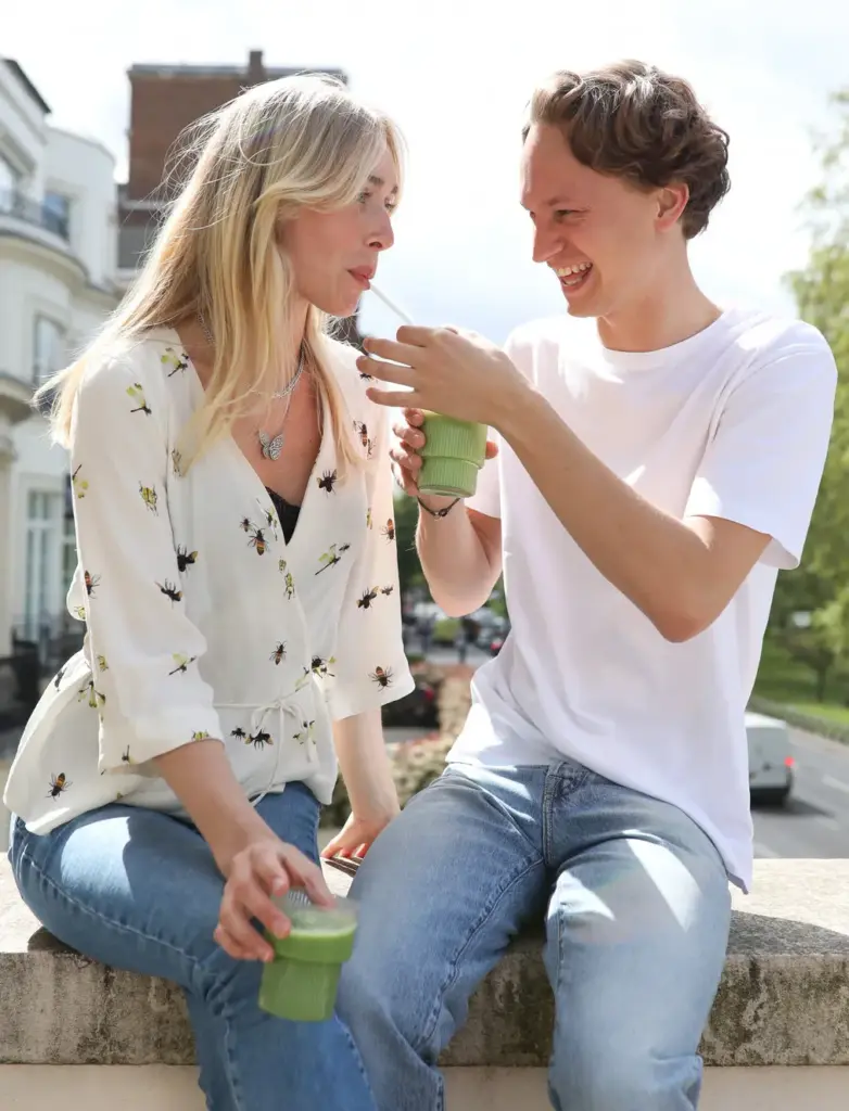 Two people seated outdoors, smiling and sipping green matcha drinks from ribbed cups