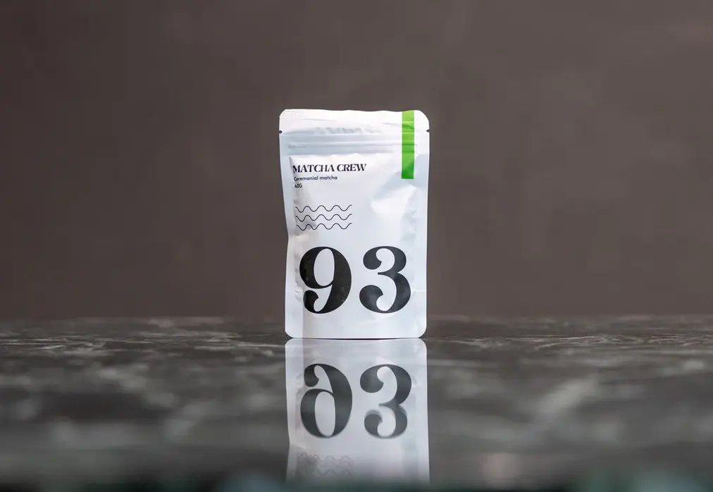 White Matcha Crew No. 93 ceremonial matcha pouch standing on a reflective dark surface