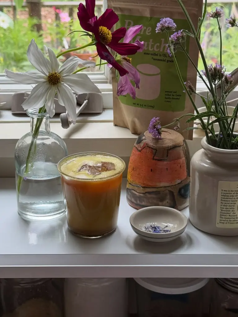 Iced drink, Pure Matcha pouch, and assorted flowers arranged by a window