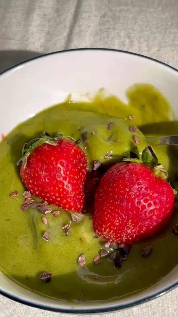 Thick green bowl topped with two strawberries and cacao nibs