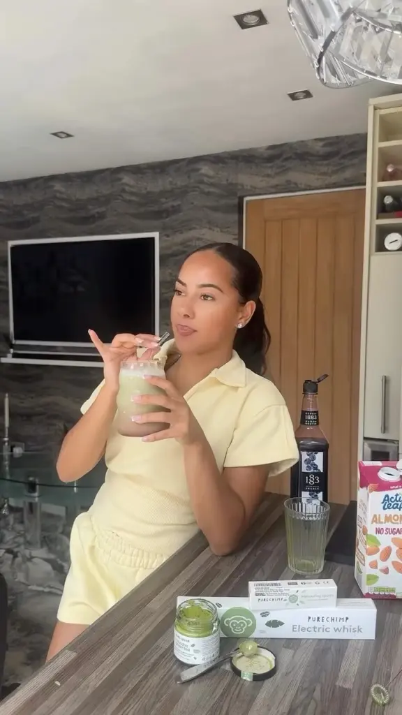 Woman holding a green drink beside PureChimp matcha and an electric whisk box