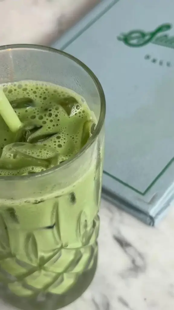 Frothy green drink with ice and a straw in a clear glass