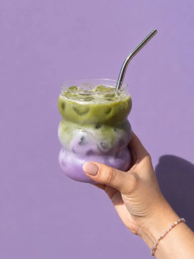 Hand holding a layered green and purple iced drink with a metal straw