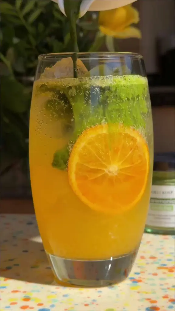 Fizzy orange and green drink with a citrus slice in a tall glass