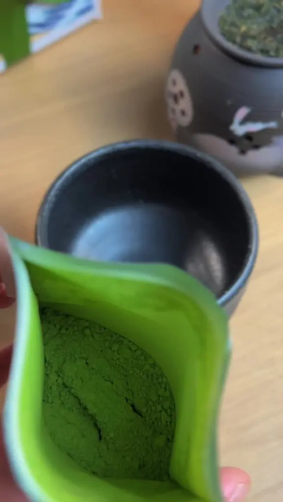 Green tea powder inside an open green-lined pouch beside a dark bowl