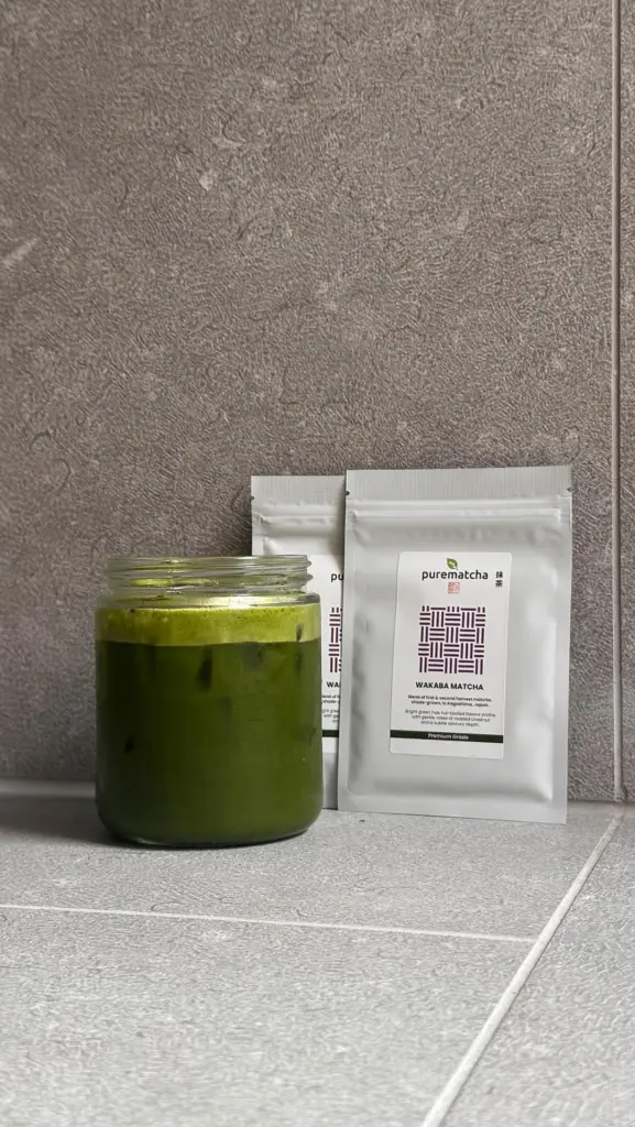 Glass jar of iced green matcha beside two Wakaba Matcha pouches