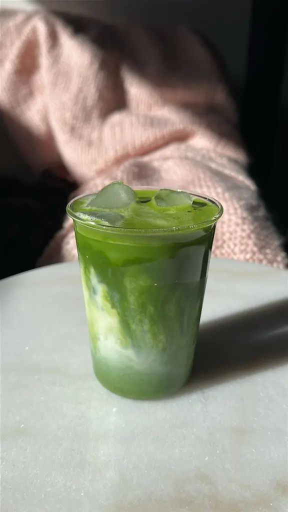 Layered green matcha and milk drink with ice in a clear cup