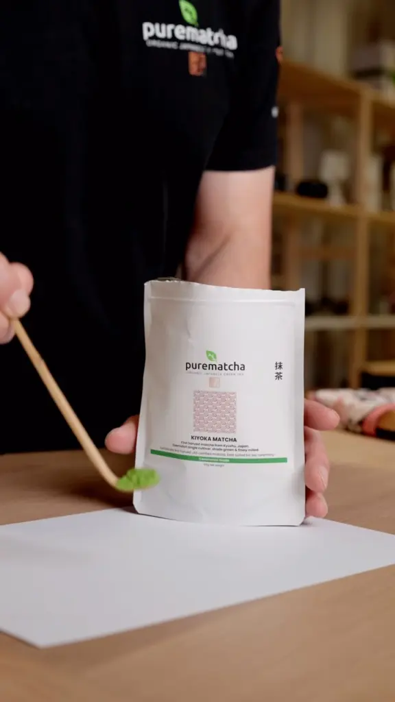 Person holding a Kiyoka Matcha pouch and a wooden spoon of green matcha powder