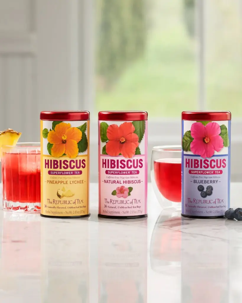Pineapple Lychee, Natural Hibiscus, and Blueberry Hibiscus tea tins with glasses of red tea