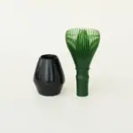 Green resin matcha whisk beside a glossy black stand
