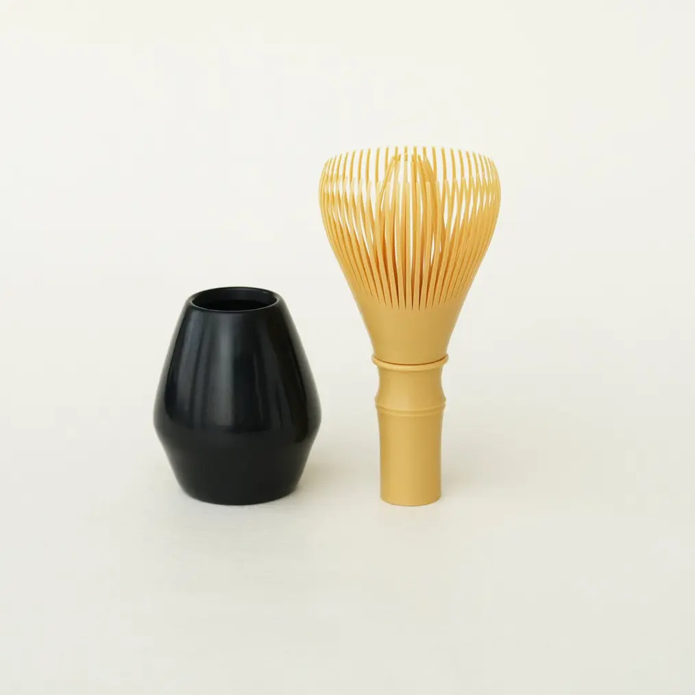 Ivory-colored resin matcha whisk beside a black whisk stand