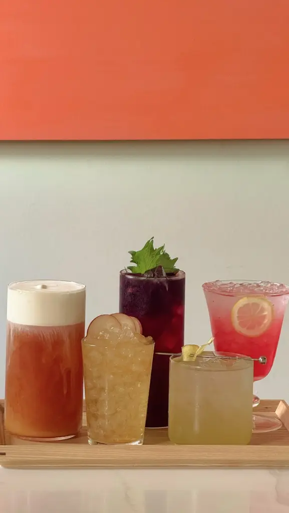 Five colorful iced drinks with fruit and leafy garnishes on a wooden tray