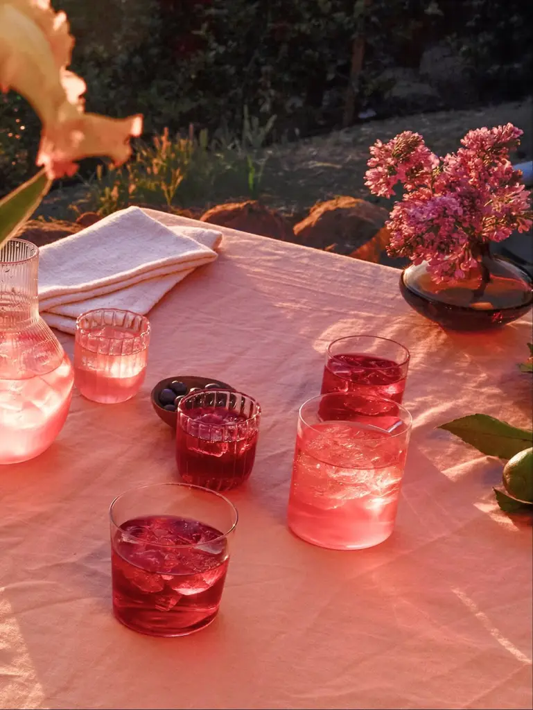 Red and pink iced drinks arranged on a sunlit table with flowers