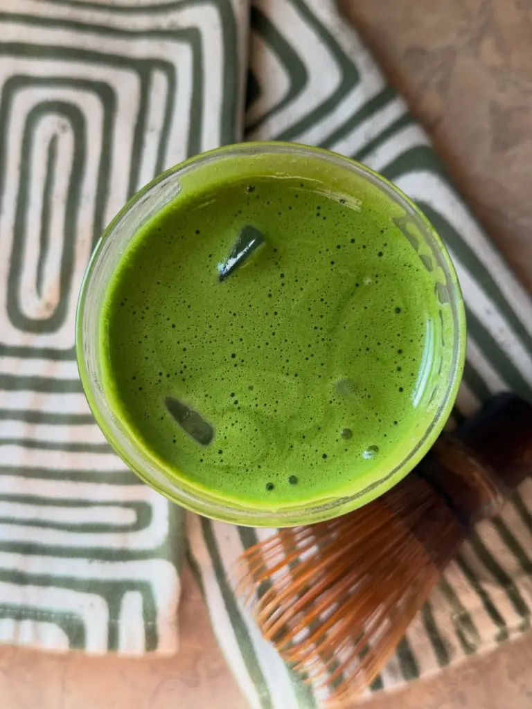 Bright green iced drink beside a bamboo whisk on patterned cloth