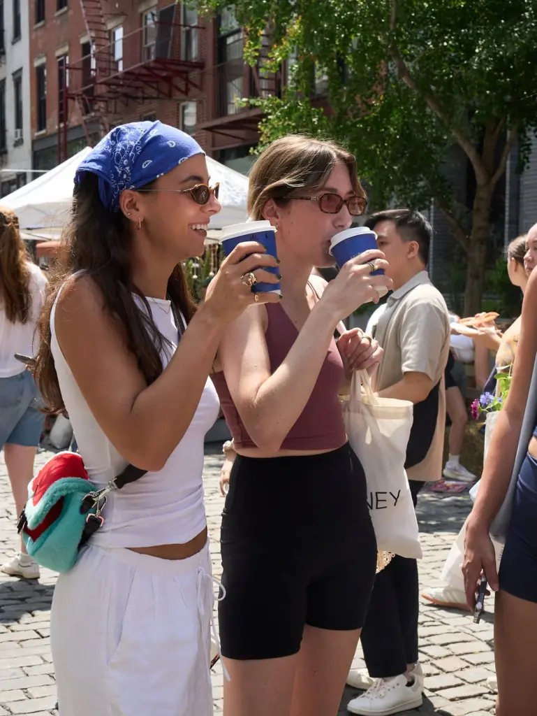 Two women in sunglasses holding blue cups at an outdoor market