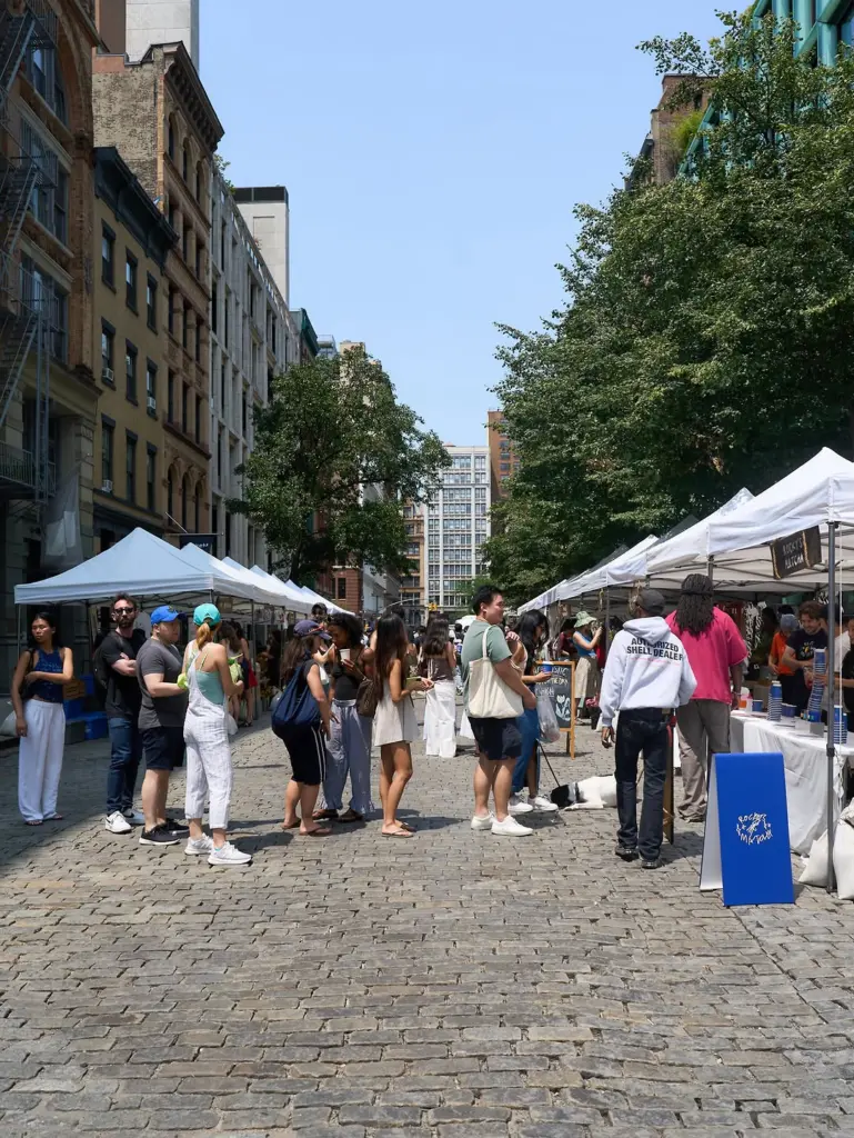 Crowd browsing white market tents on a sunny cobblestone street