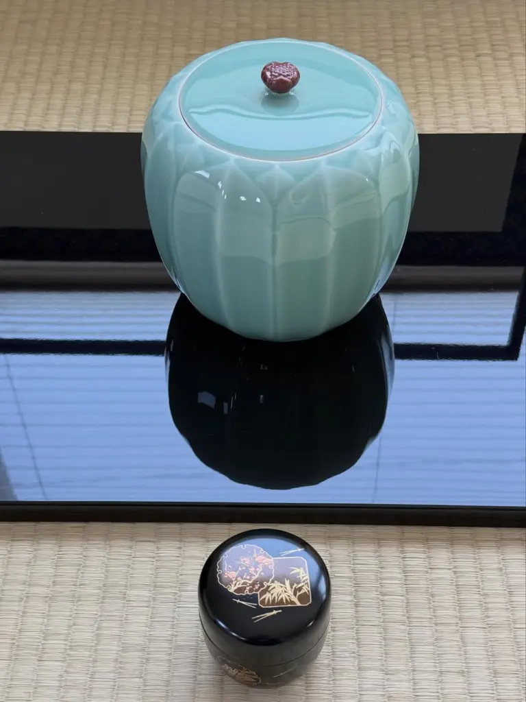 Pale blue-green lidded jar and small decorated black container on tatami
