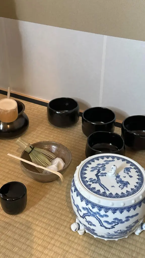 Black tea bowls, bamboo whisk, ladle, and blue-and-white lidded jar on tatami