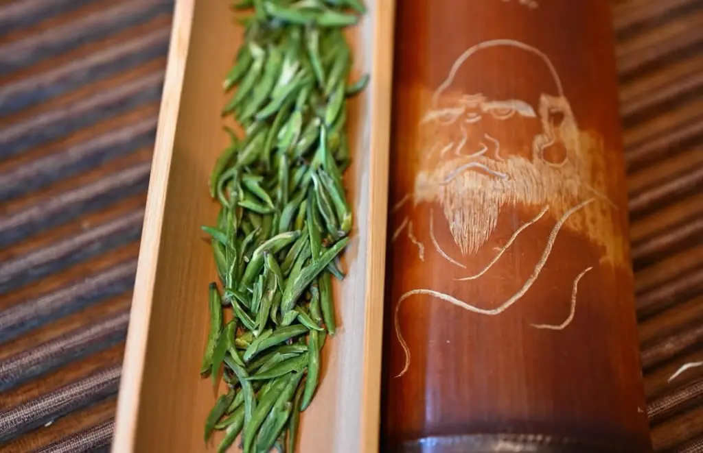 Green tea leaves beside a bamboo container etched with a bearded face