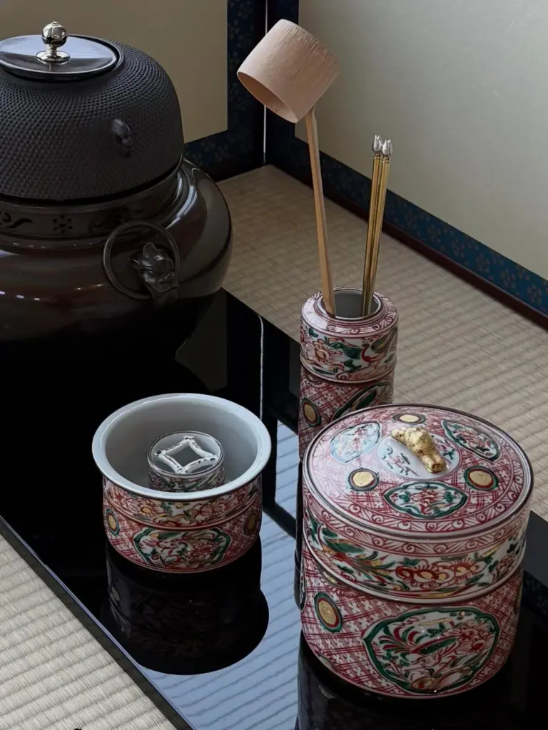 Patterned ceramic tea containers and utensils beside a dark iron kettle