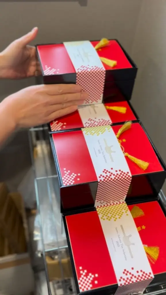 Hands arranging stacked red gift boxes with patterned bands and gold tassels
