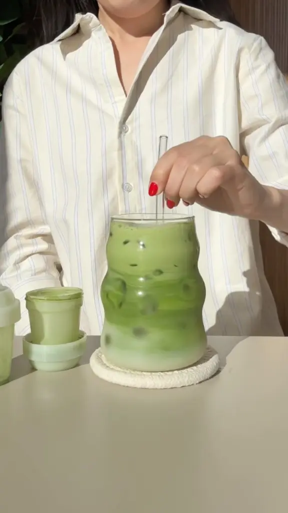 Person stirring a layered iced green drink in a glass