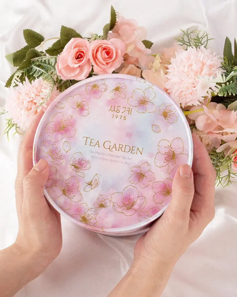 Hands holding a pink floral Tea Garden tin among pale pink flowers