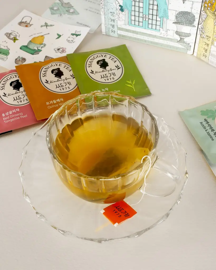 Glass cup of amber tea surrounded by colorful Ssanggye Tea sachets