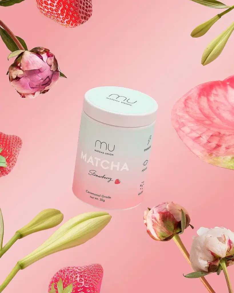 Matcha Union Strawberry Matcha tin surrounded by strawberries and pink flowers on a pink background
