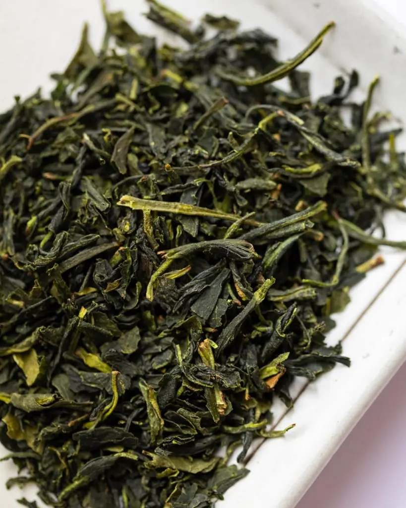 Close-up of dark green dried tea leaves on a white tray