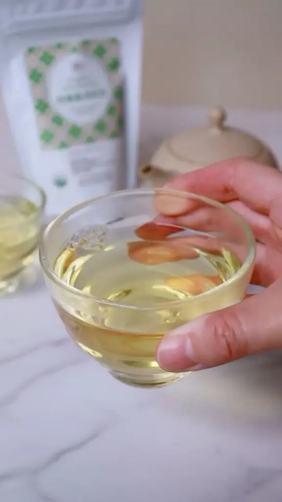 Hand holding a clear glass cup filled with pale yellow tea