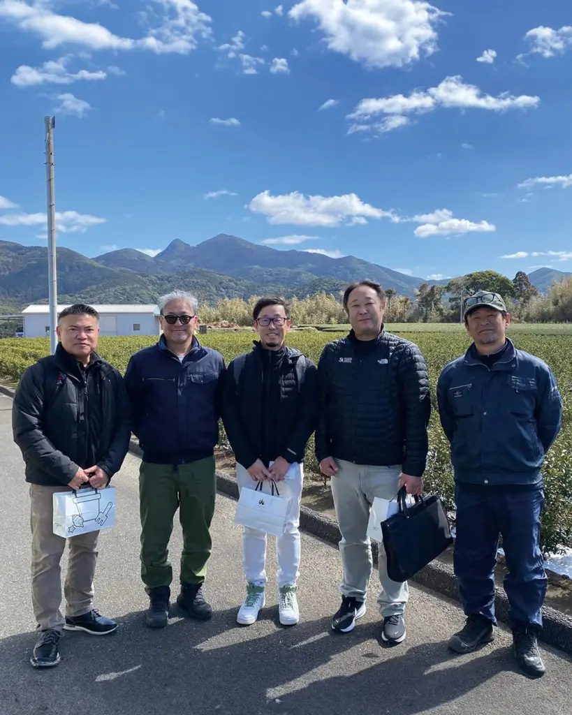 Five men standing beside a green tea field with mountains behind them