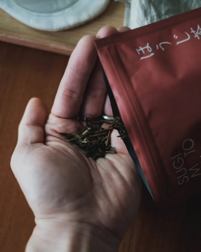 Loose roasted tea leaves poured from a red packet into an open hand