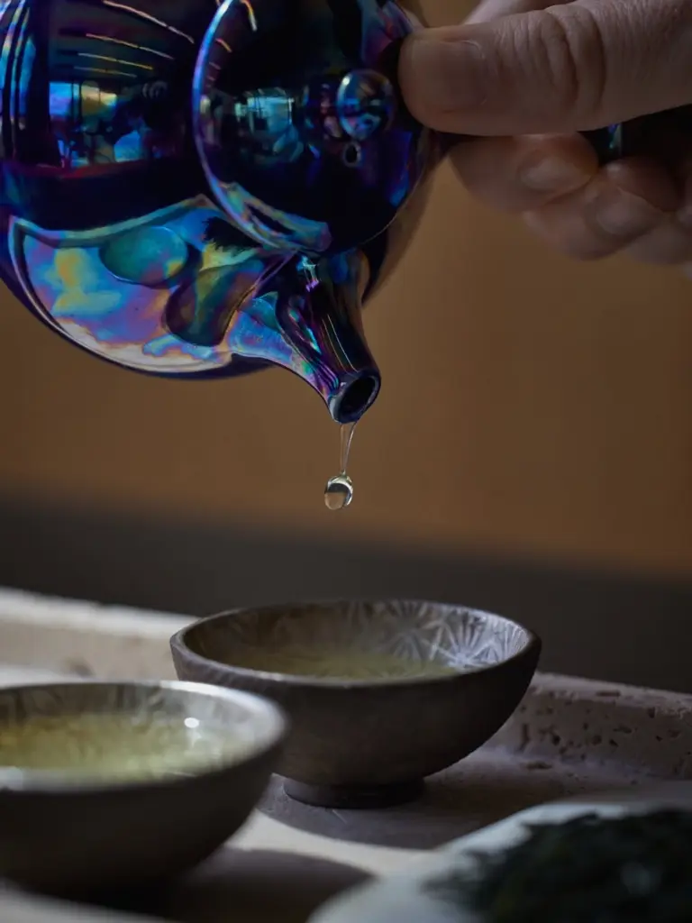 Hand pouring tea from an iridescent teapot into a ceramic cup