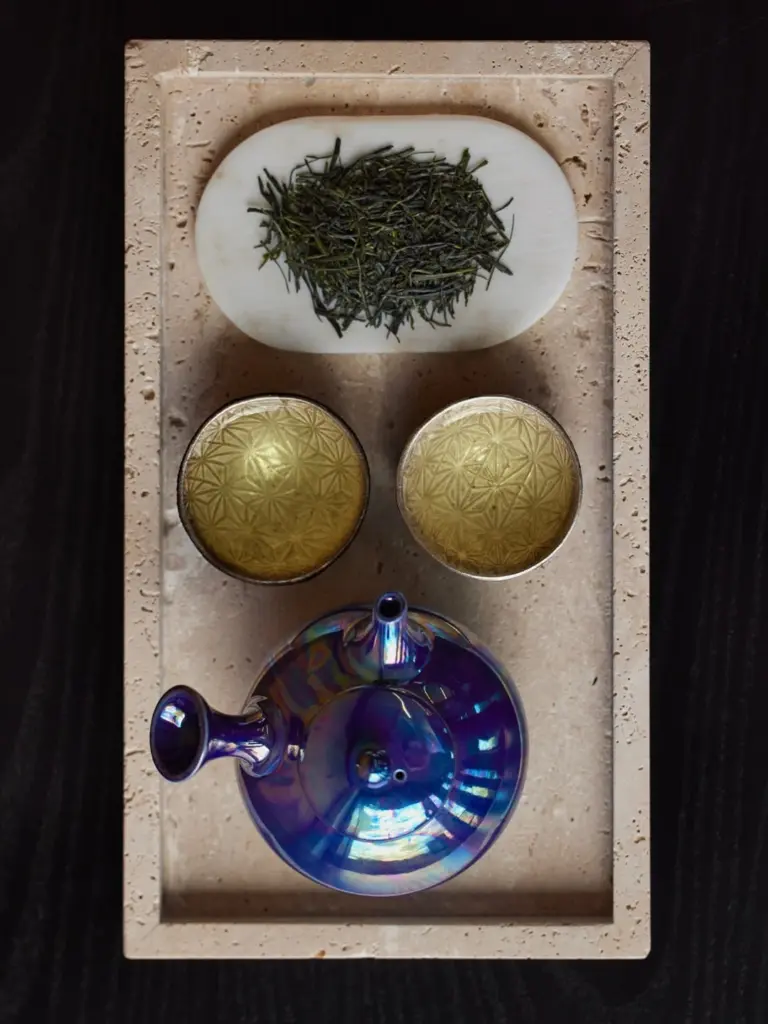 Iridescent teapot, two filled cups, and loose tea leaves on a tray