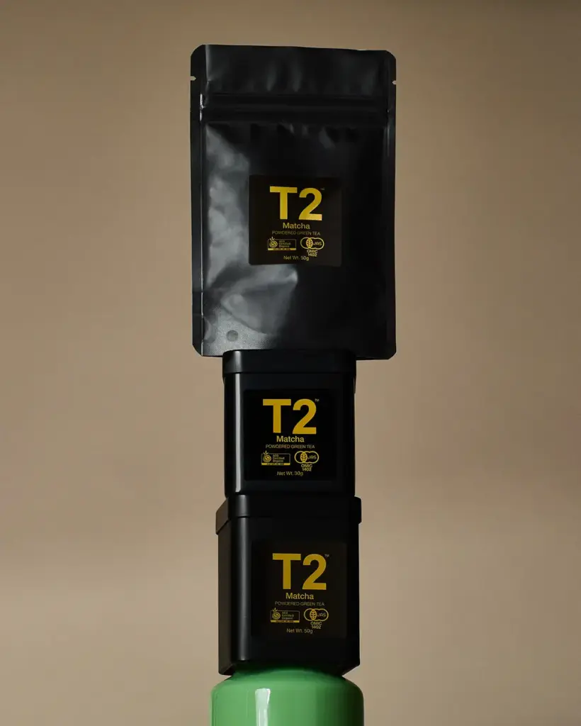 Black T2 Matcha pouch and two tins stacked vertically against a tan background