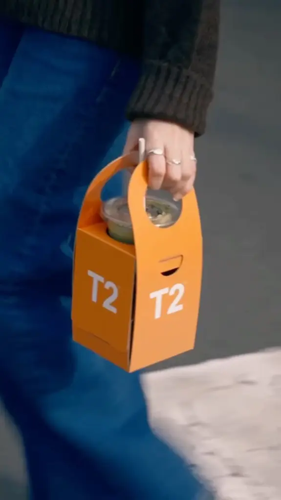 Person carrying an orange T2 drink holder with a lidded cup inside