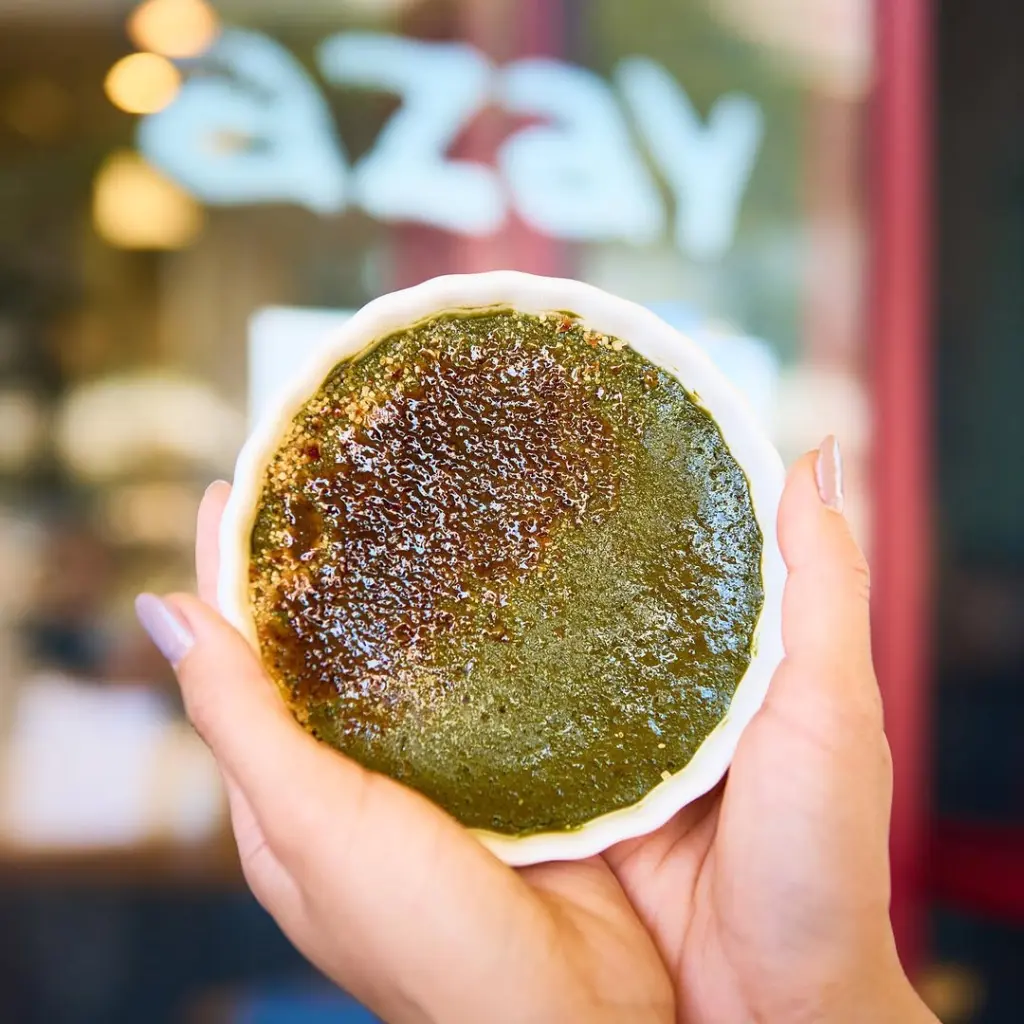 Hands holding a green dessert with a caramelized top