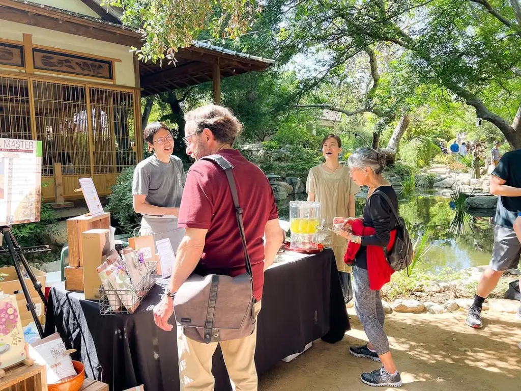 Visitors gathered around an outdoor tea table beside a garden pond