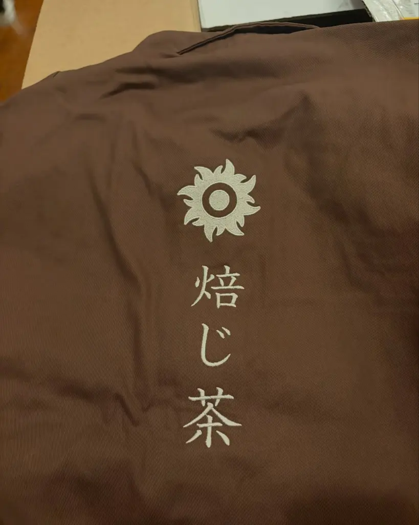 Cream emblem and Japanese characters embroidered on brown fabric