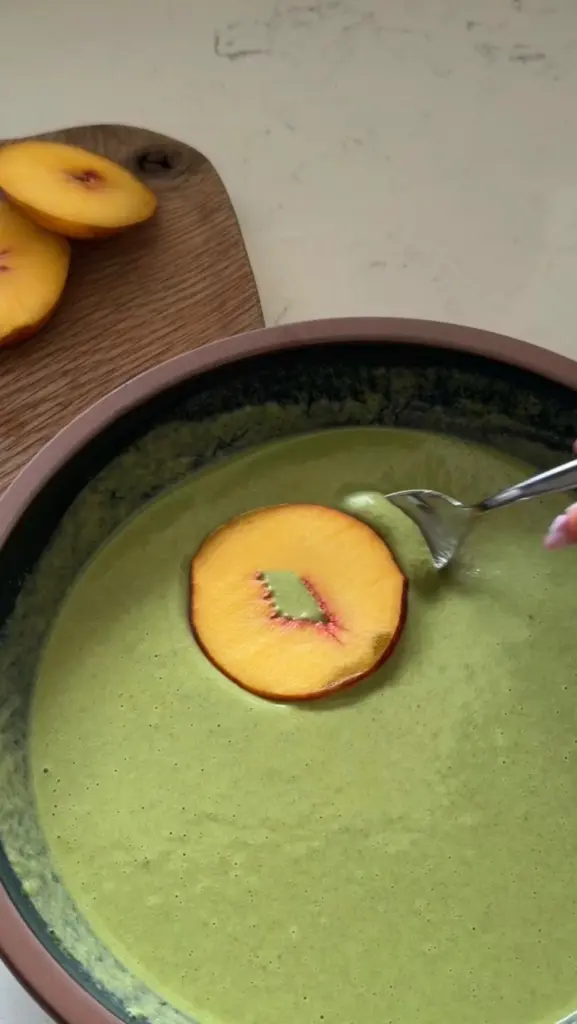 Creamy green mixture in a bowl topped with a peach slice