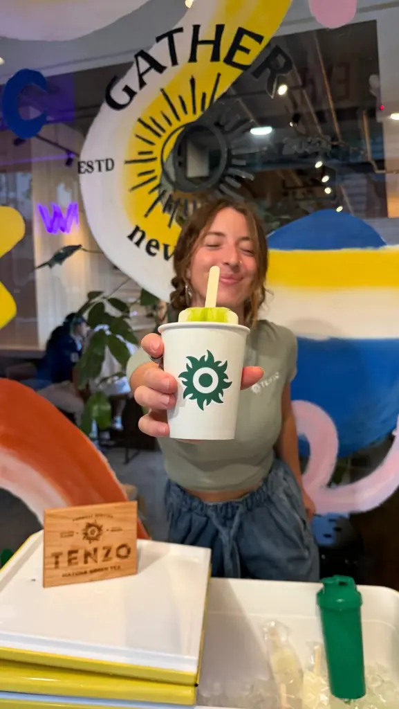 Smiling woman presenting a green frozen treat in a paper cup