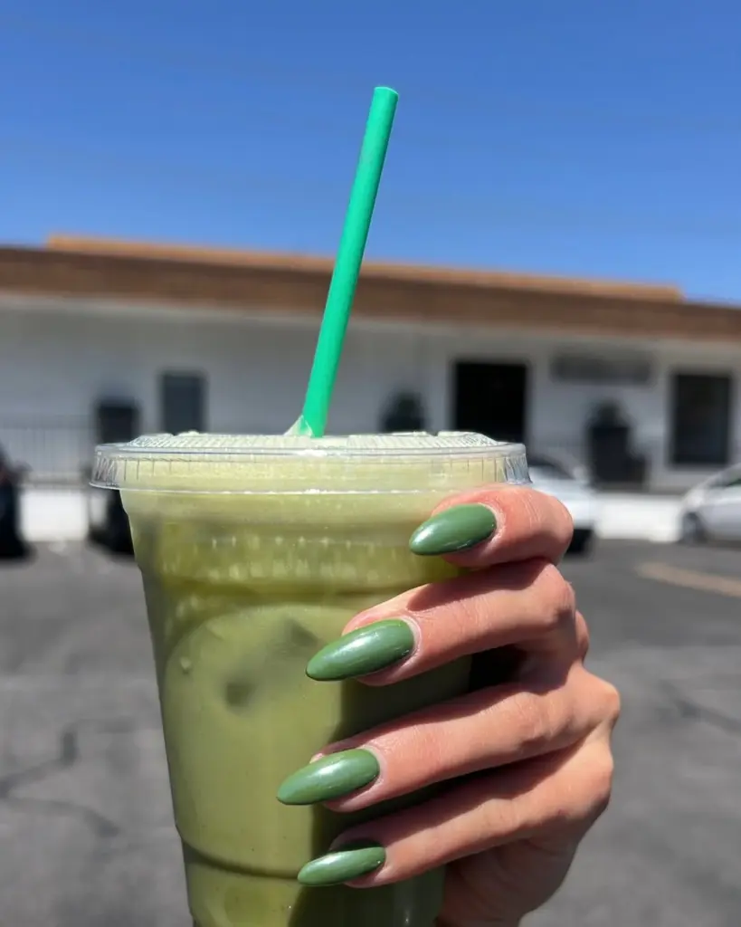 Hand with glossy green nails holding an iced green drink outdoors