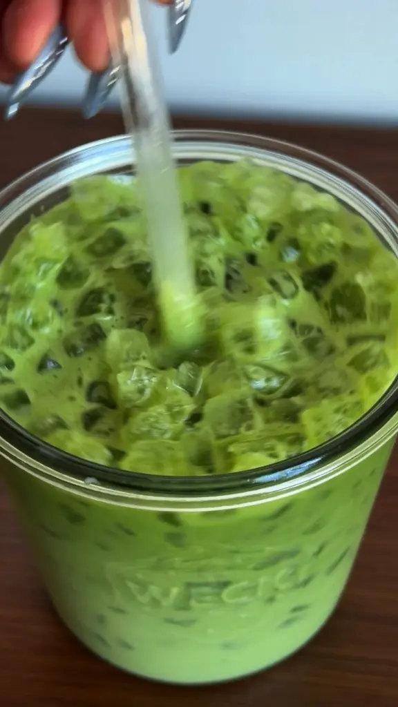 Bright green iced drink being stirred in a clear glass