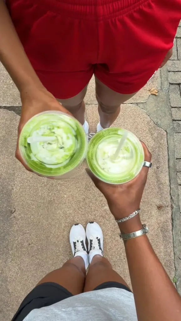 Two people holding iced green drinks with creamy swirls