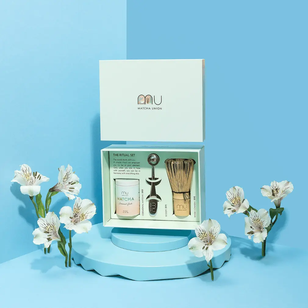 Open Matcha Union Ritual Set with matcha tin, metal scoop, and bamboo whisk on a blue floral display